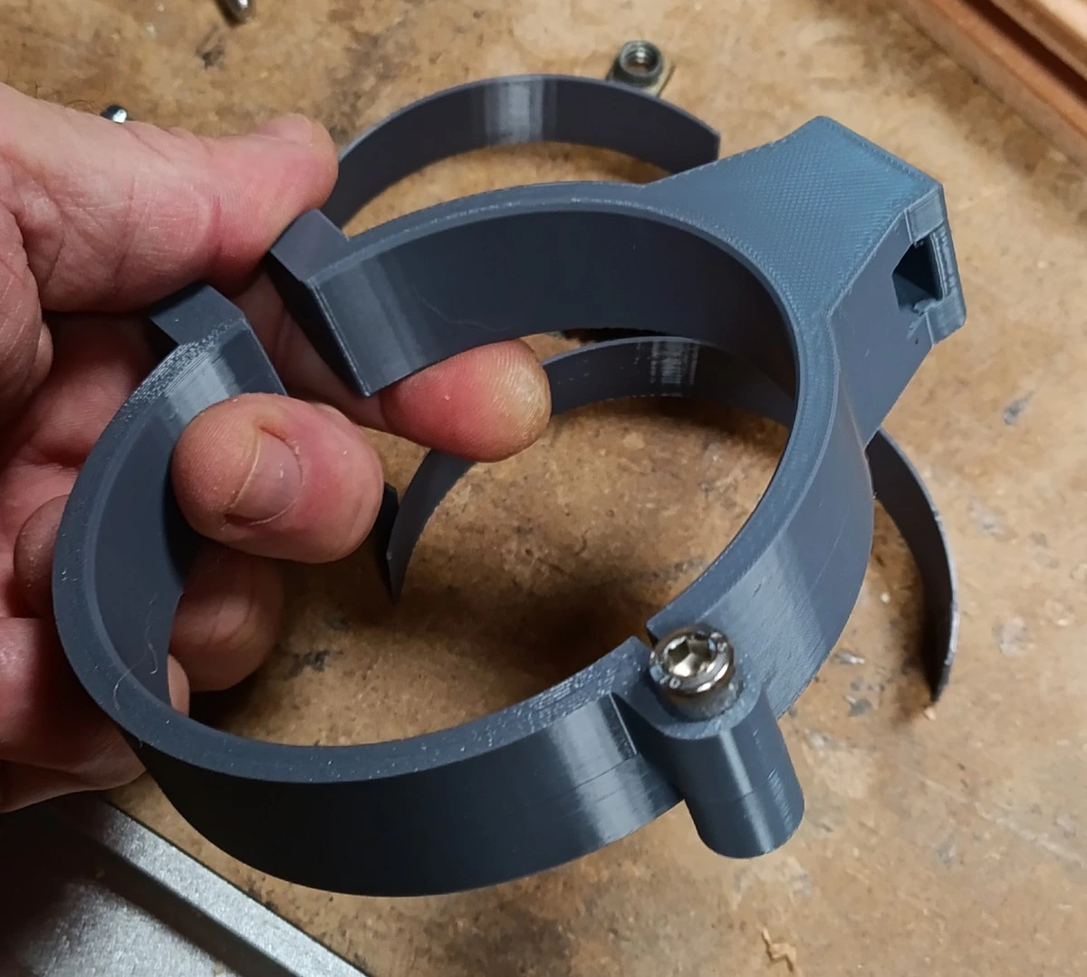 Le collier tenu en main, ouvert : les deux demi-anneaux imprimés s'emboîtent par leur charnière à deux nœuds, la vis inox du côté opposé