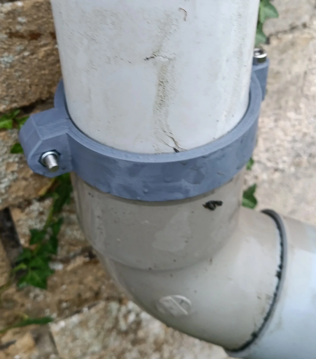 Le collier gris imprimé en place sur la descente blanche, juste au-dessus du coude, contre un mur de pierre couvert de lierre